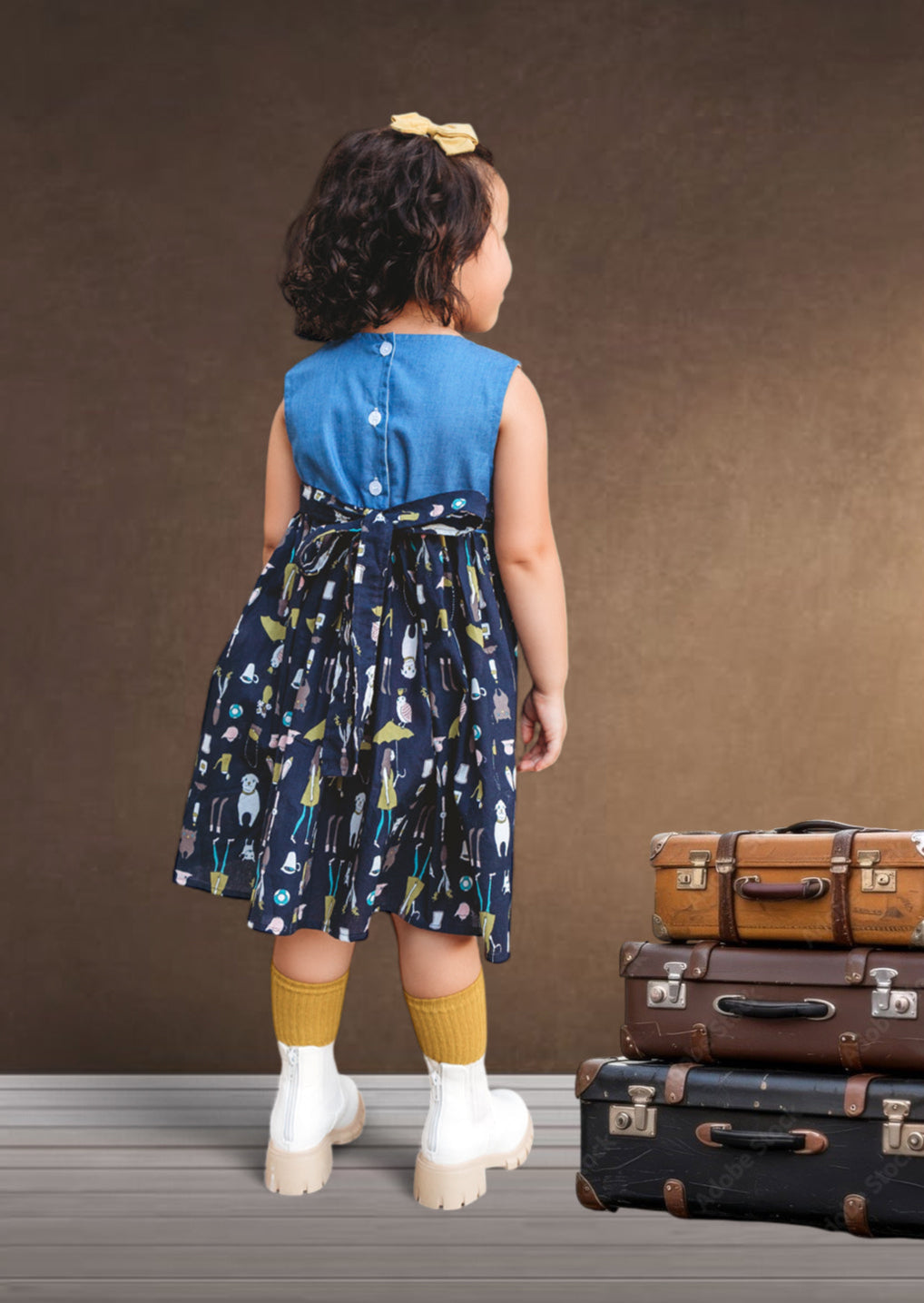 Child in a blue dress standing next to vintage suitcases against a brown background